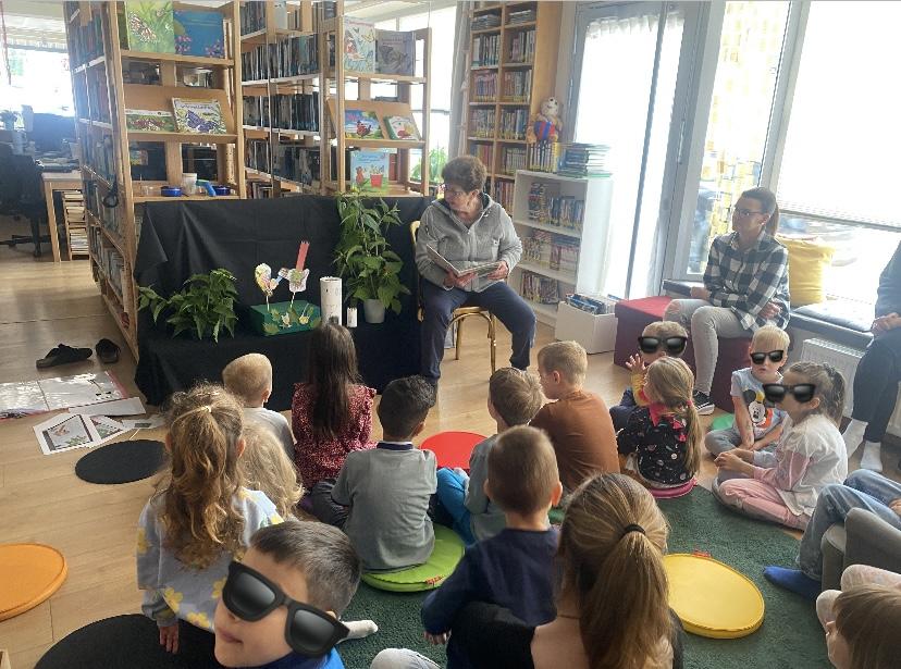 viele Kinder sitzen am Boden und lassen sich eine Geschichte vorlesen