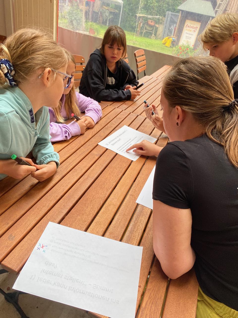 Eine Gruppe Kinder sitzen am Tisch und studieren einen Zettel