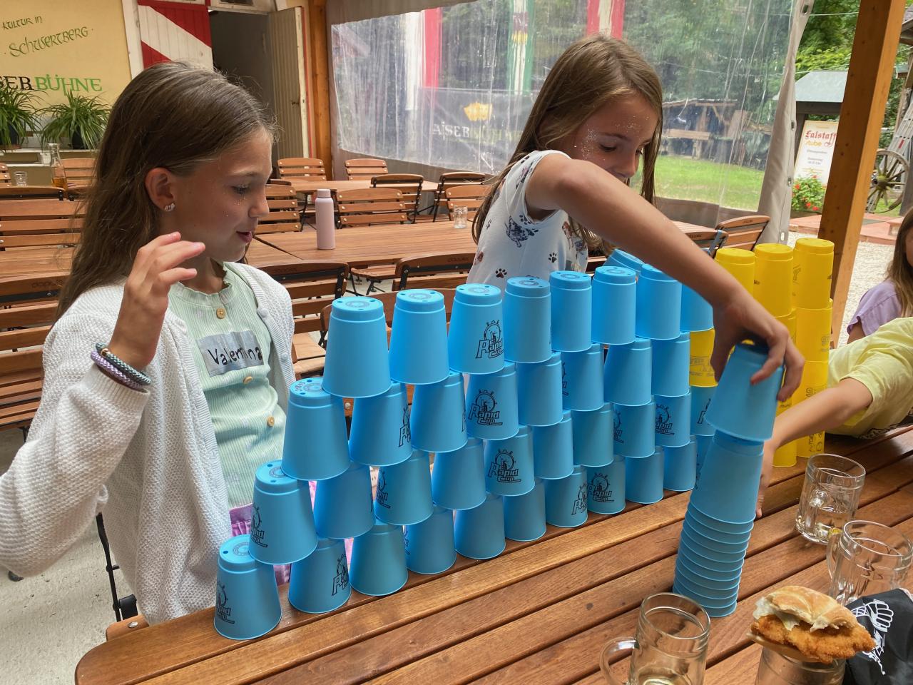 Zwei Mädchen hinter einem Turm aus Plastikbechern