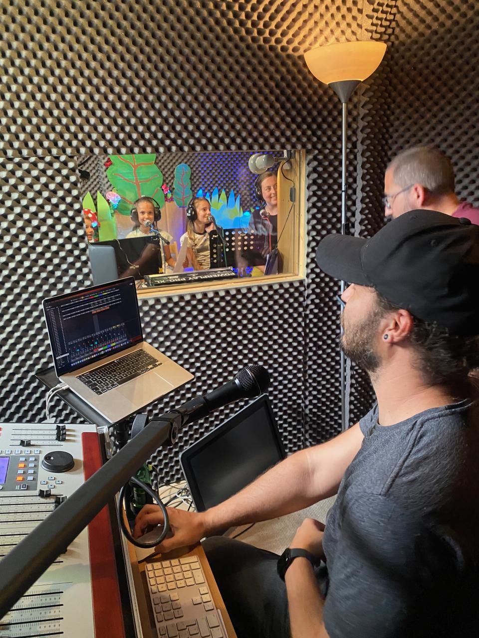 Ein Mann beobachtet drei Kinder im Tonstudio durch ein Fenster