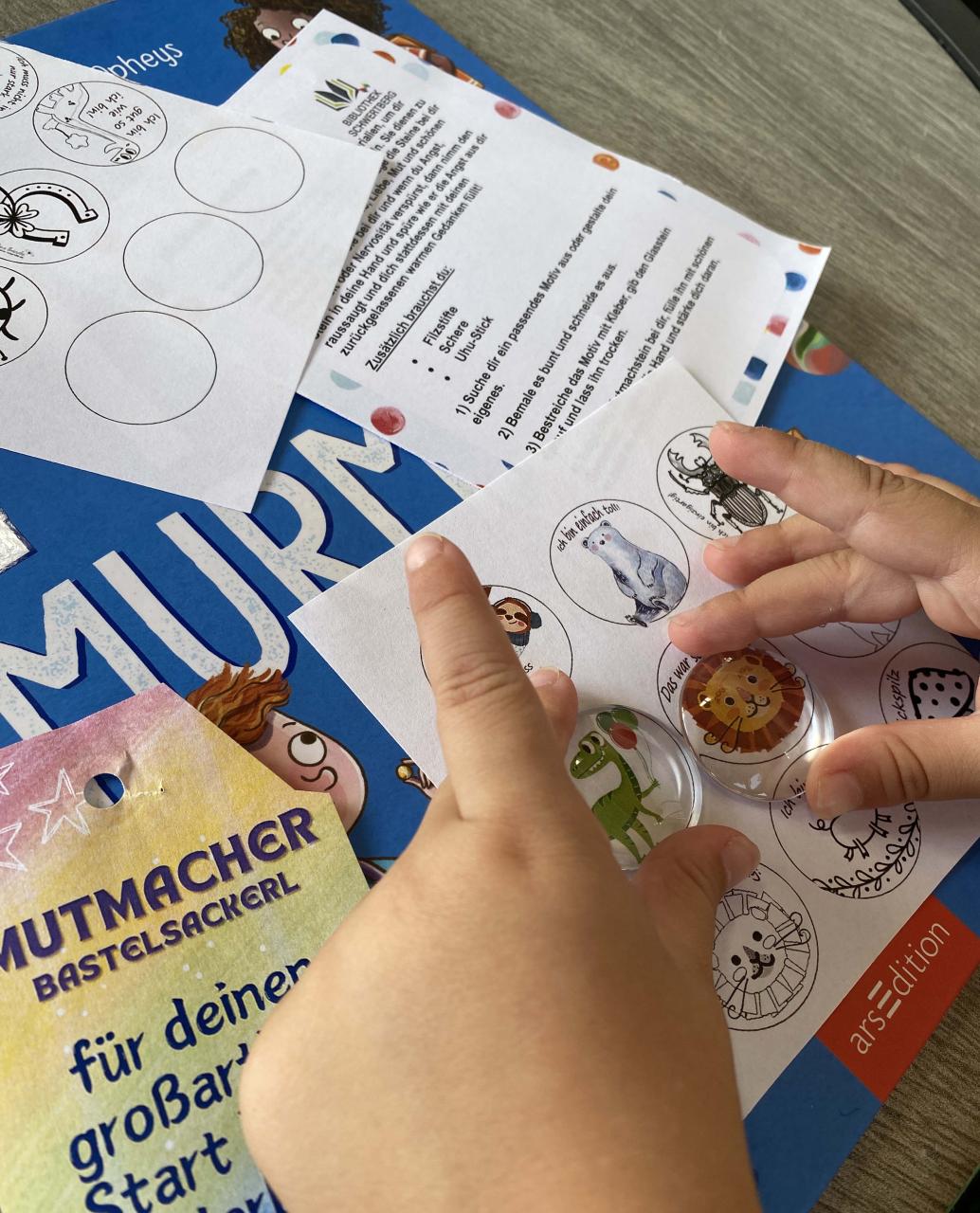 Zwei Kinderhände halten zwei Glassteine auf eine Zeichnung