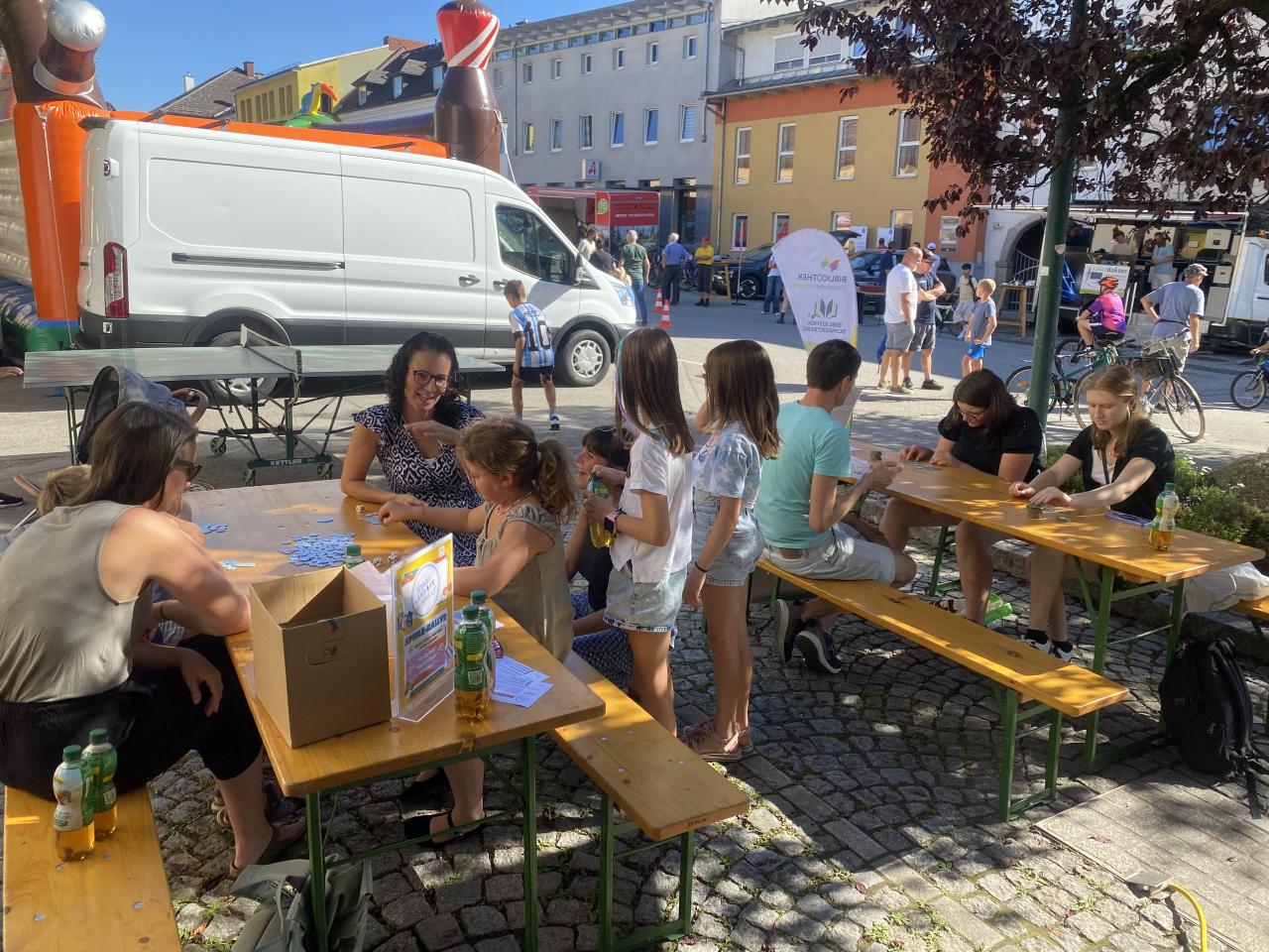 Menschen sitzen vor der Bibliothek auf Bänken und spielen