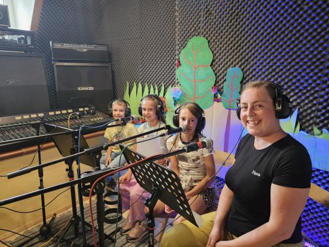Drei Kinder und eine Frau im Tonstudio mit Kopfhörer