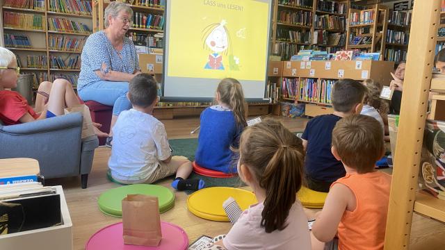 Kinder sitzen vor einer Leinwand und nebenbei die Vorleserin