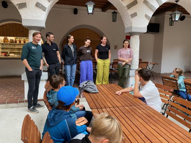 Einige Kinder sitzen am Tisch, Erwachsene stehen dahinter