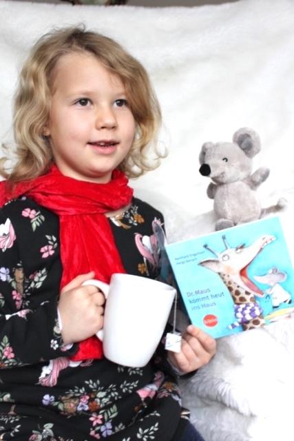 Ein Mädchen mit einem Buch, einer Tasse und einer Stoffmaus