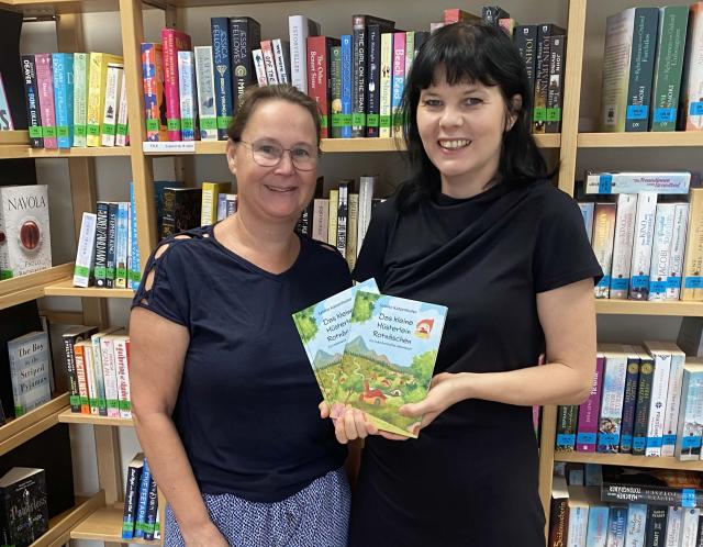 Zwei Frauen vor einer Bücherwand mit einem Kinderbuch in der Hand