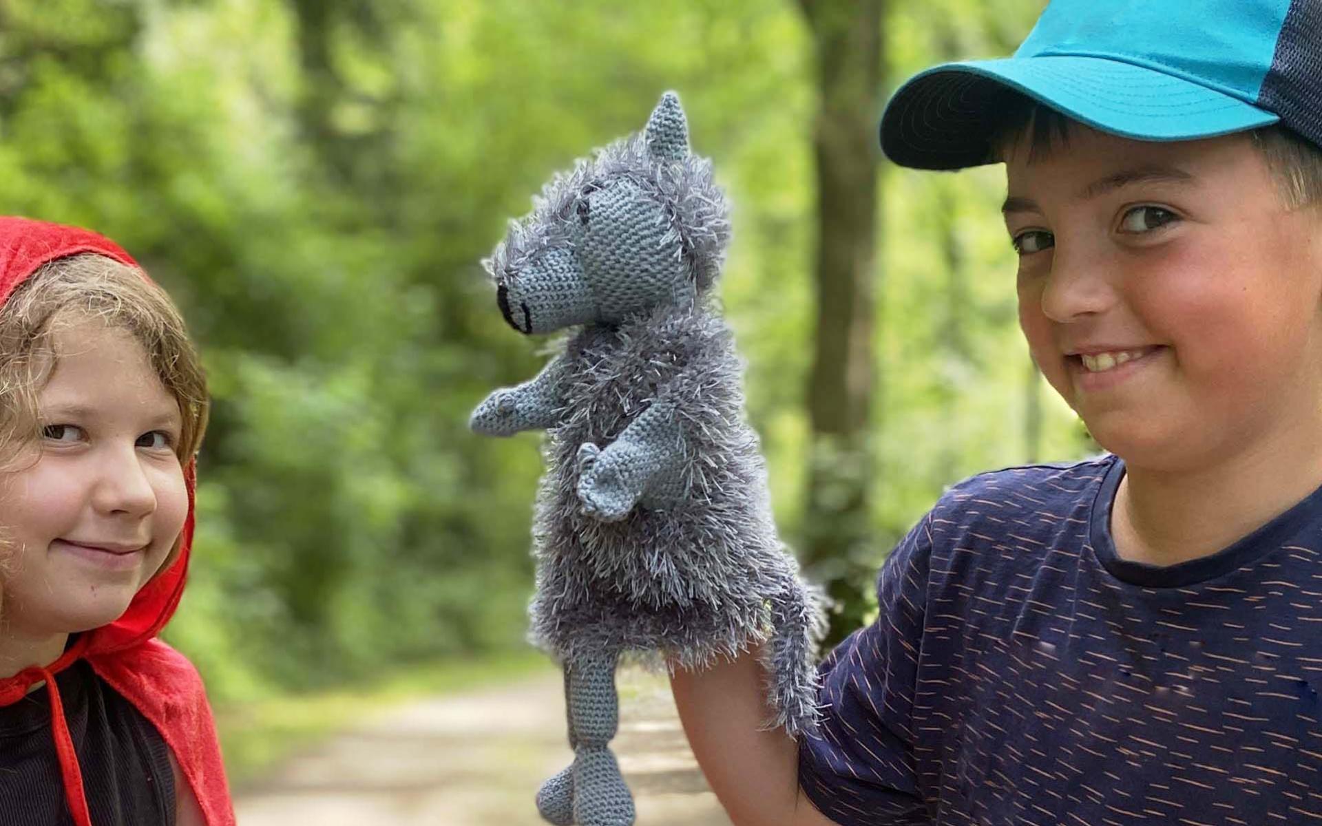 Ein Mädchen mit Rokäppchenumhang und eine Junge mit einer Wolfshandpuppe