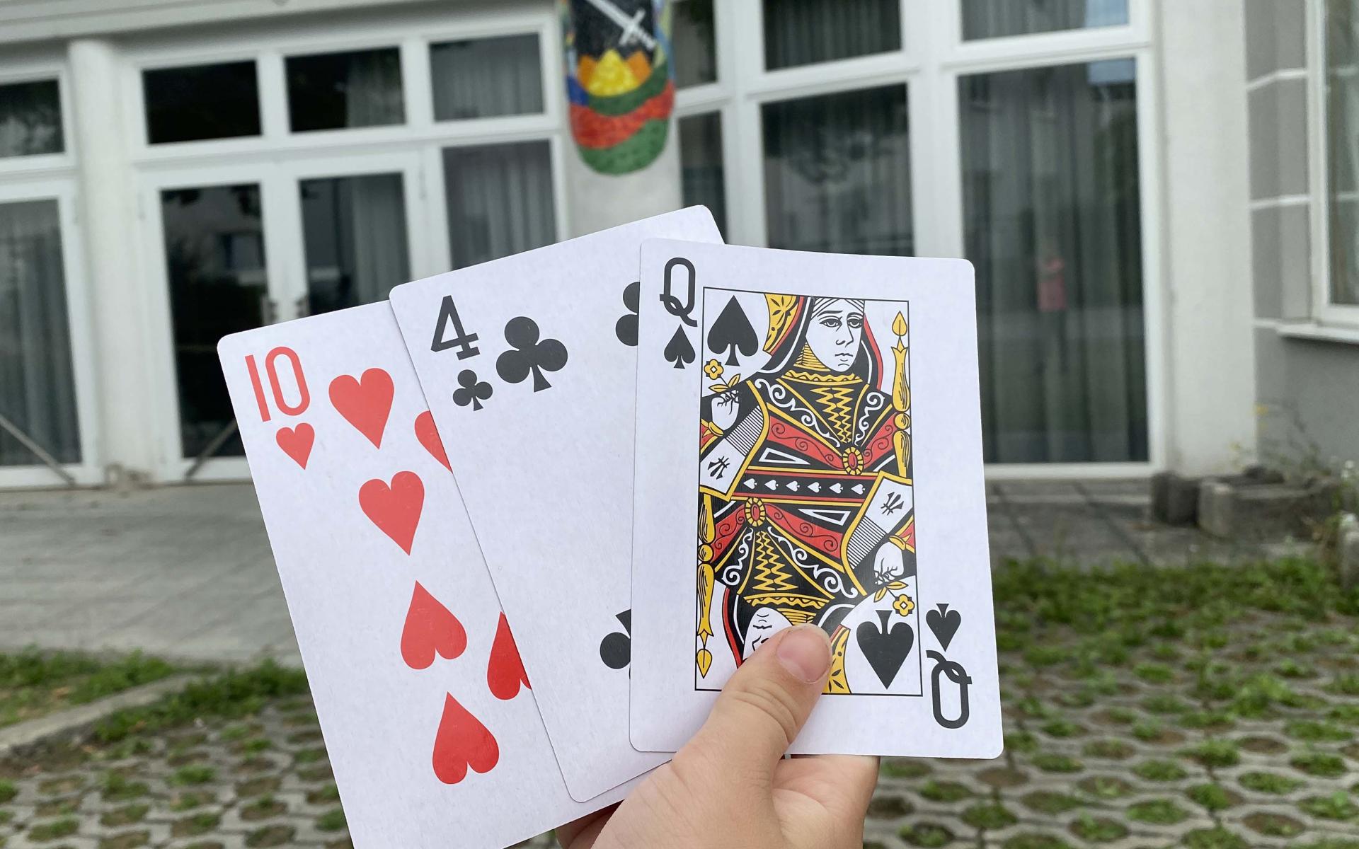 Hand hält Spielkarten vor dem Volksheim Schwertberg