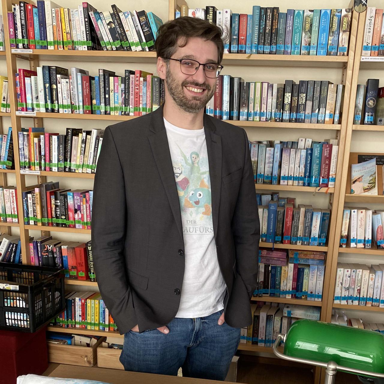 Ein Mann steht hinter Werbeartikel, dahinter ein Bücherregal