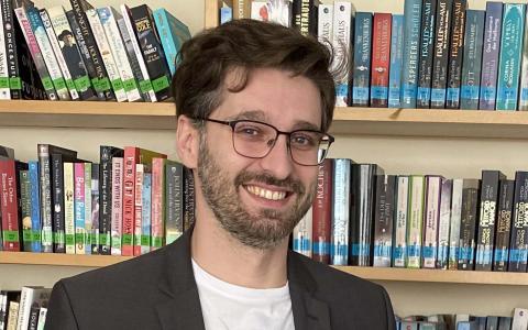 Ein Mann steht hinter Werbeartikel, dahinter ein Bücherregal