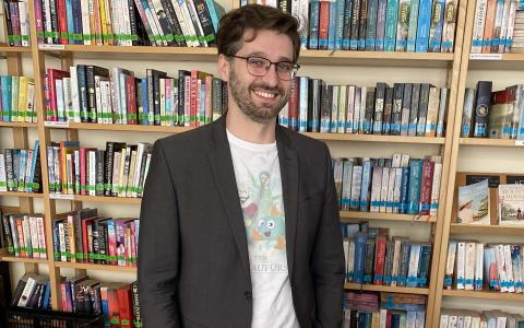 Ein Mann steht hinter Werbeartikel, dahinter ein Bücherregal